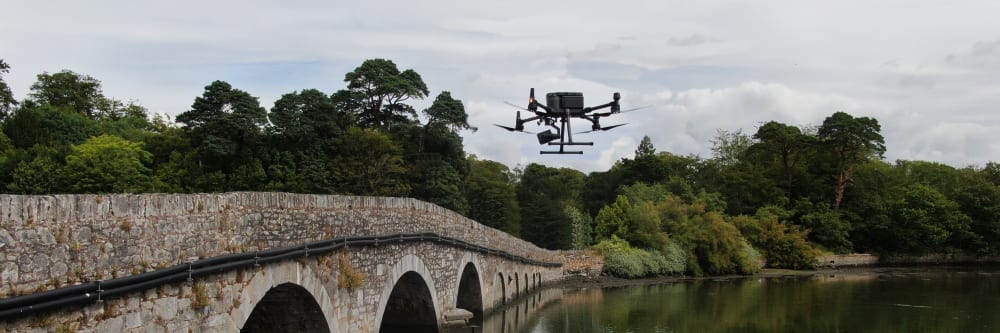 A UAV performing a drone bridge inspection on an old stone road bridge