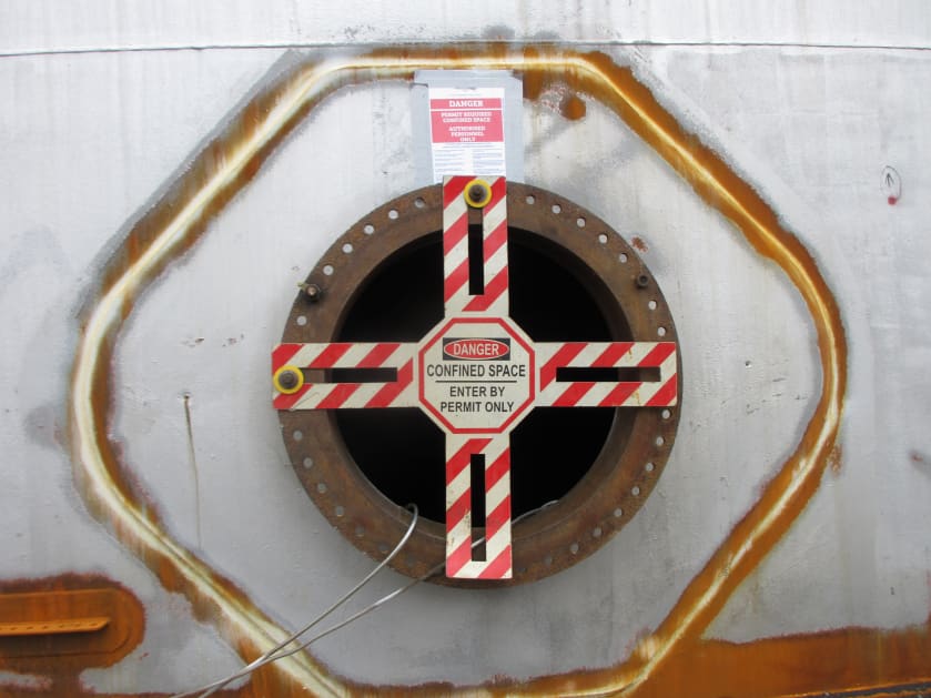 The man way of a large steel storage tank which is labeled as a confined space..