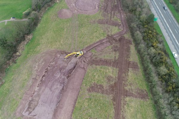 A drone view of an excavator cutting ground on an earthworks site, with spoil heaped alongside