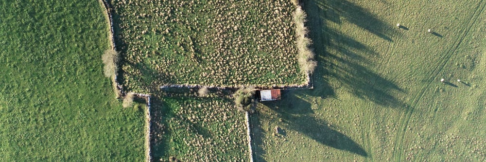 Aerial photo of scrubby farm land with a small shed and some old stone walls