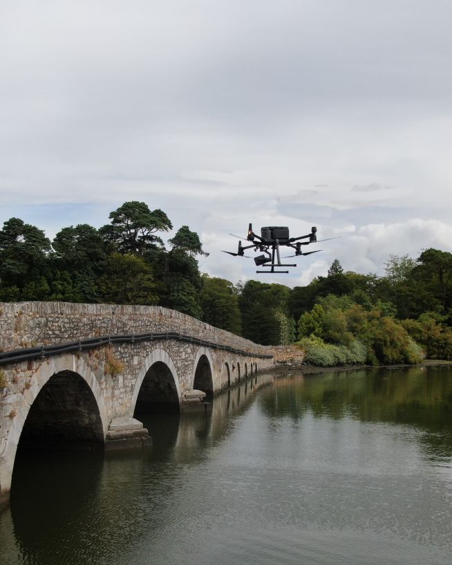 A UAV performing a drone bridge inspection on an old stone road bridge