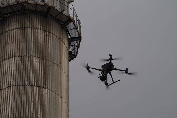 An inspection drone flying beside a tall steel-clad industrial stack
