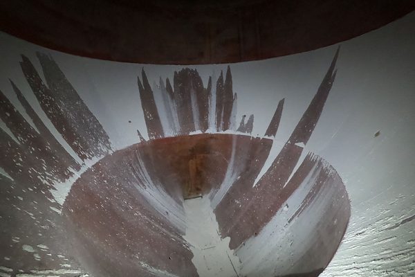 The interior surface of a cylindrical vessel, showing a large area of coating loss around a central opening